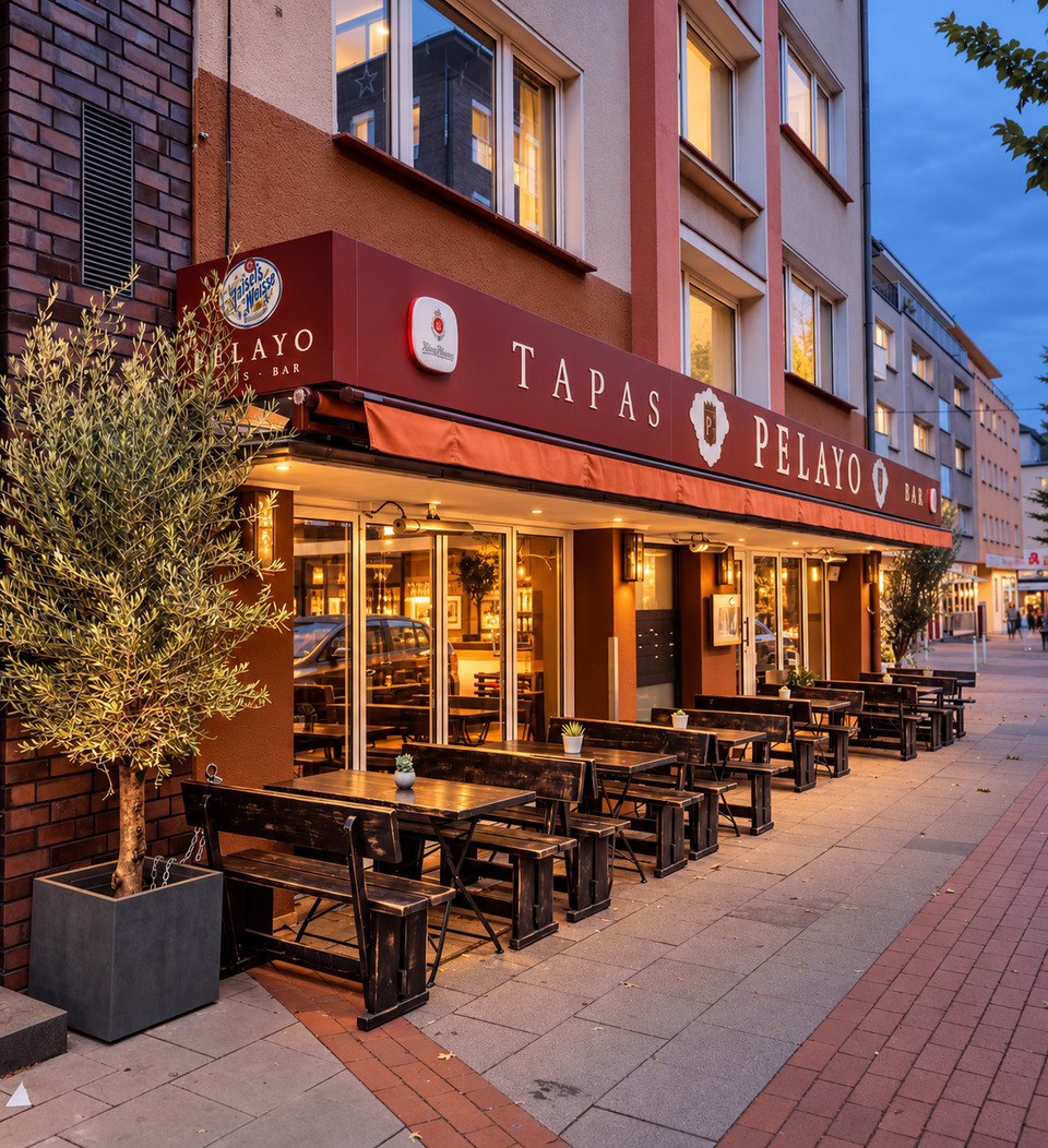 Pelayo am Abend mit roter Markise, Olivenbaum und Sitzplätzen vor dem Restaurant